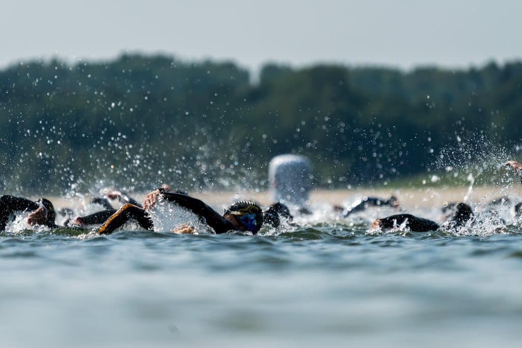 A mass swim start, dozens of open-water swimmers churning across a lake