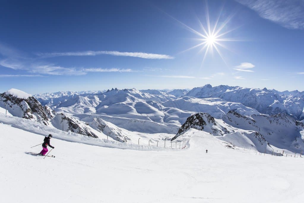 A skier traversing a high alpine ridge under blue sky